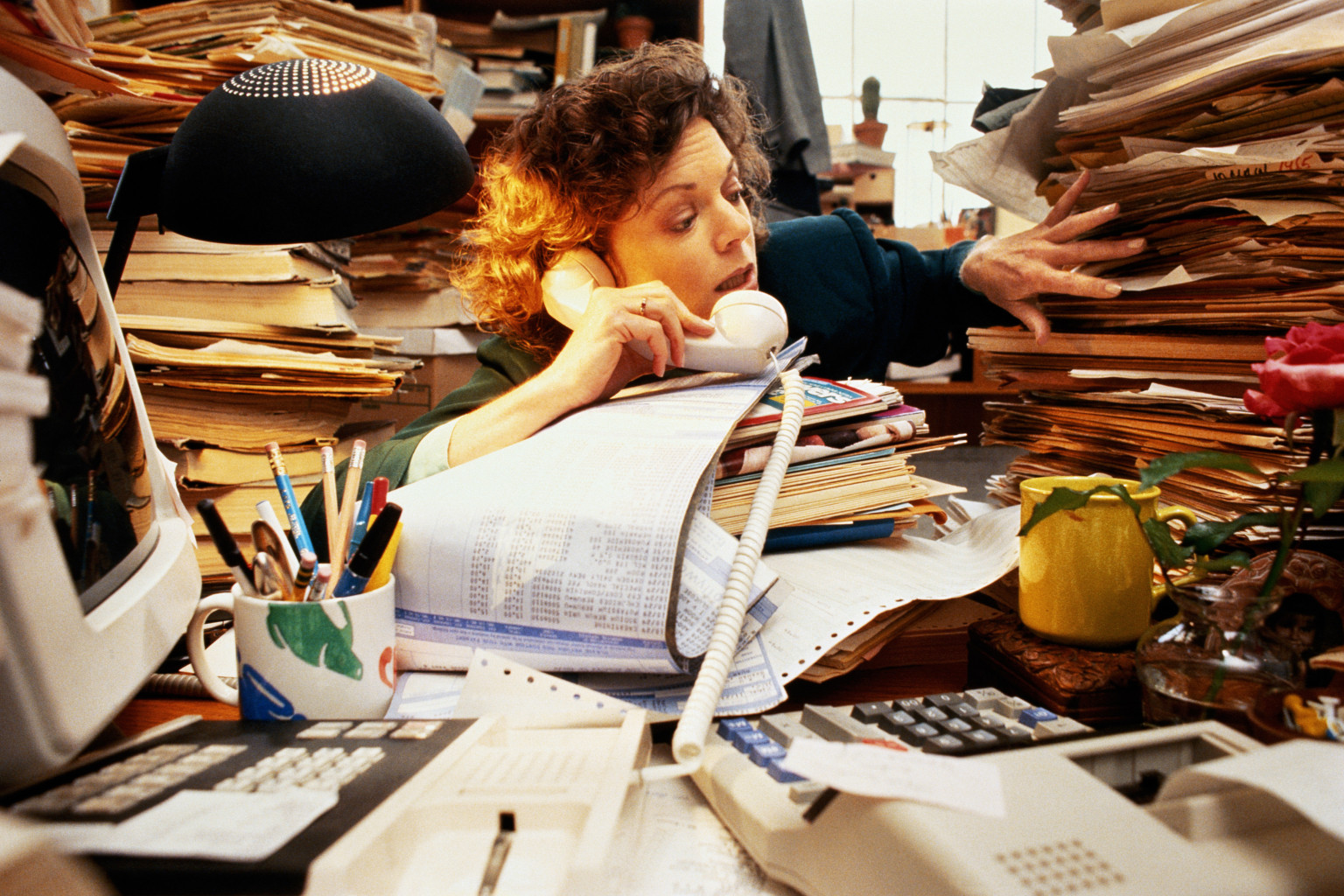 Businesswoman on phone at desk piled high with messy files
