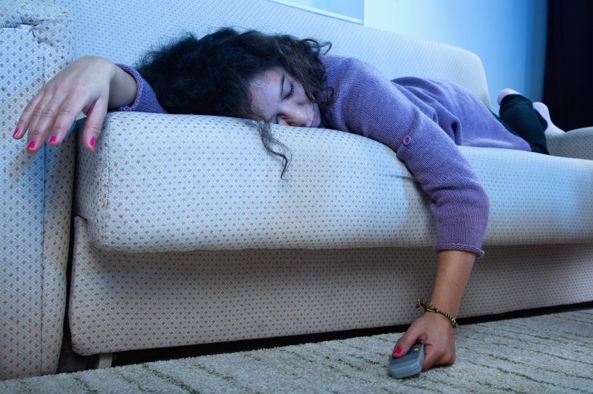 Young woman sleep on the couch in a dark living room with the TV on amd remote in hand.