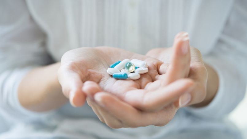 Closeup shot of a woman holding various pills on hand. Girl with white shirt showing medicines and pills indoor. Shallow depth of field with focus on pill.