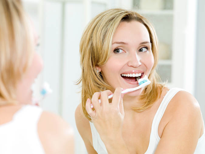 Young smiling woman cleaning teeth with toothbrush in bathroom