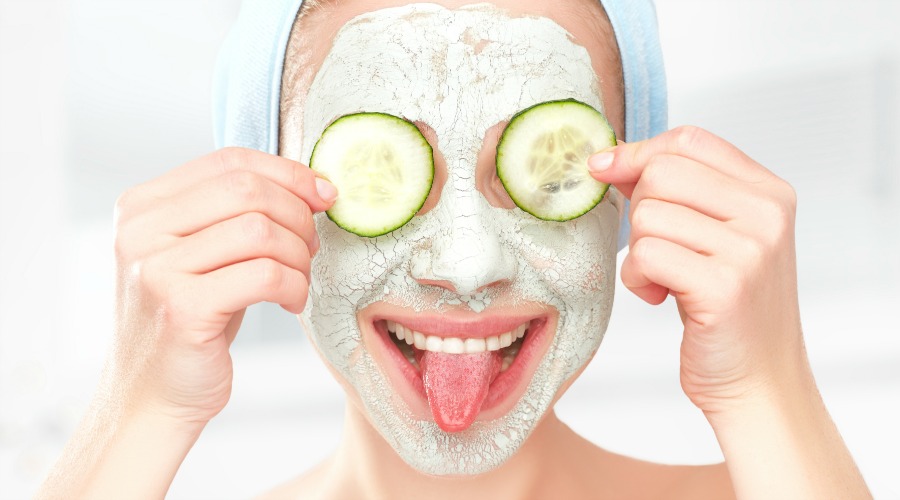 Funny young girl with a mask for skin face and cucumbers on eyes