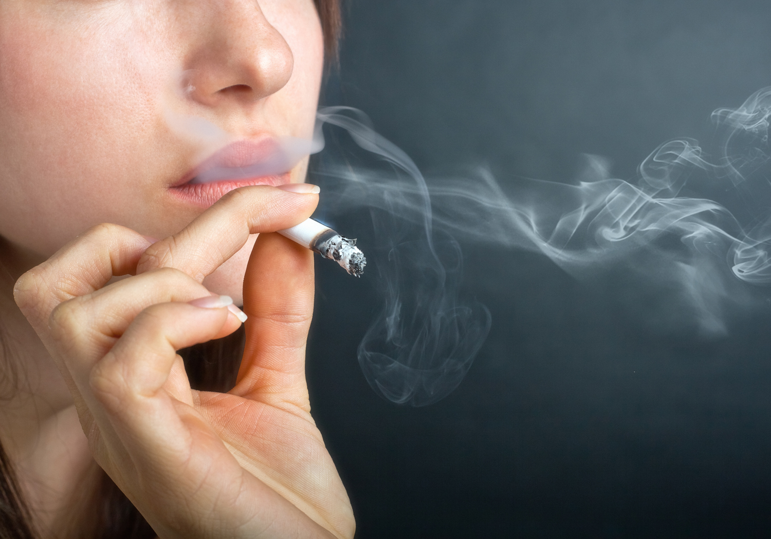 Woman with Cigarette Exhaling Smoke on a Dark Background
